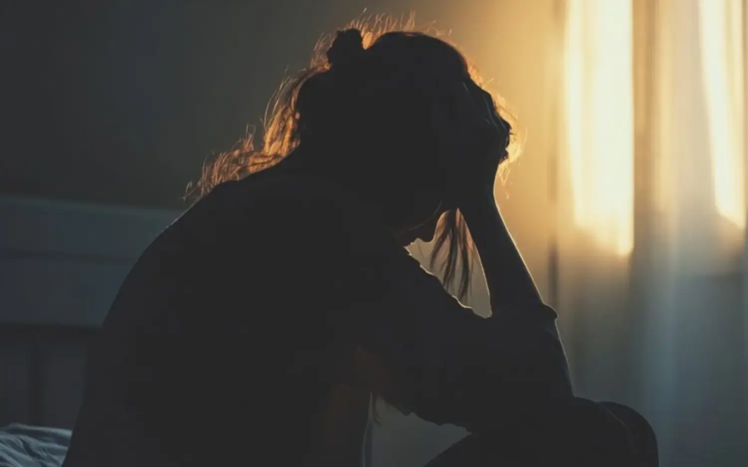 Silhouette of a woman sitting on her bed, head in hands