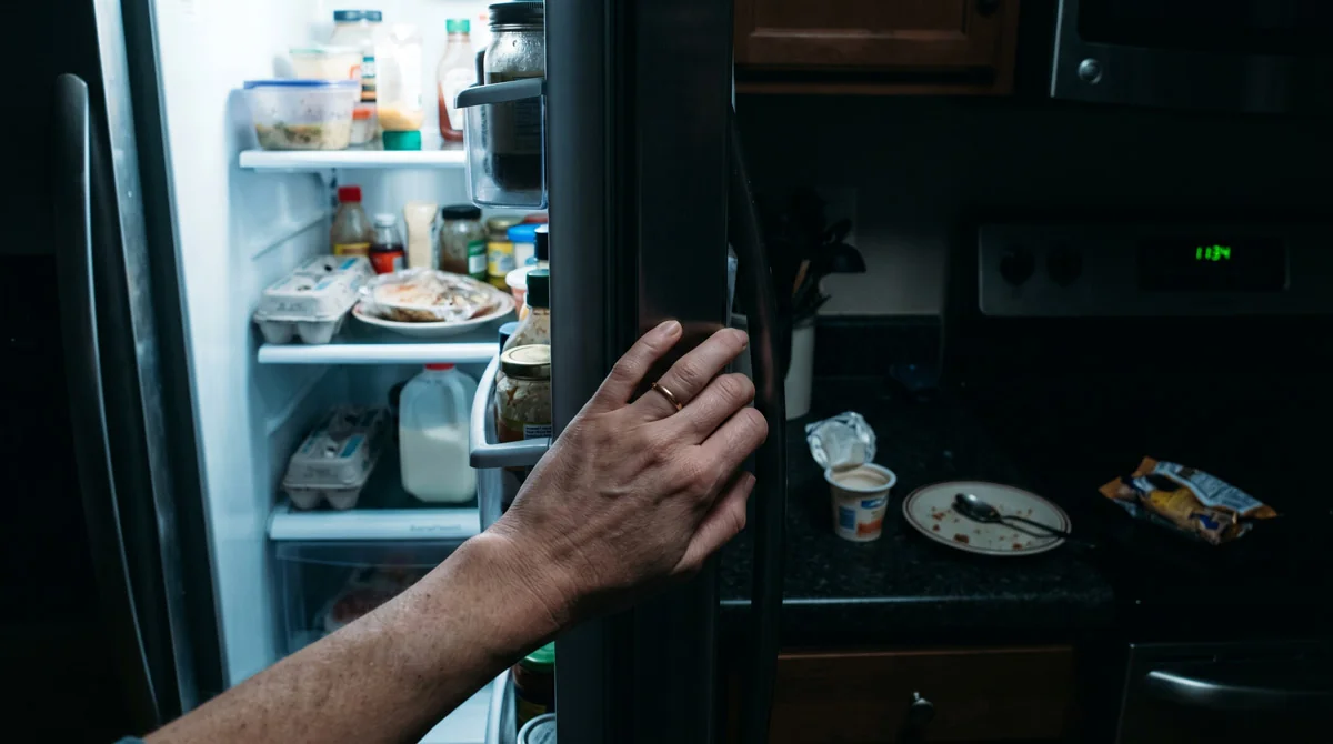 A woman opening her refrigerator late at night in a dimly lit kitchen